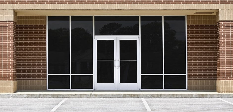 A new unoccupied generic store front, business or professional office space in a contemporary strip mall. Red brick with dark tinted windows in brushed aluminum frames and a double door.